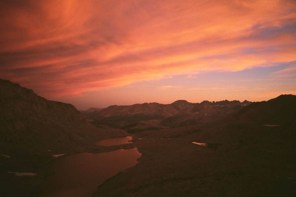 A sunset with pink clouds and mountains in the background.