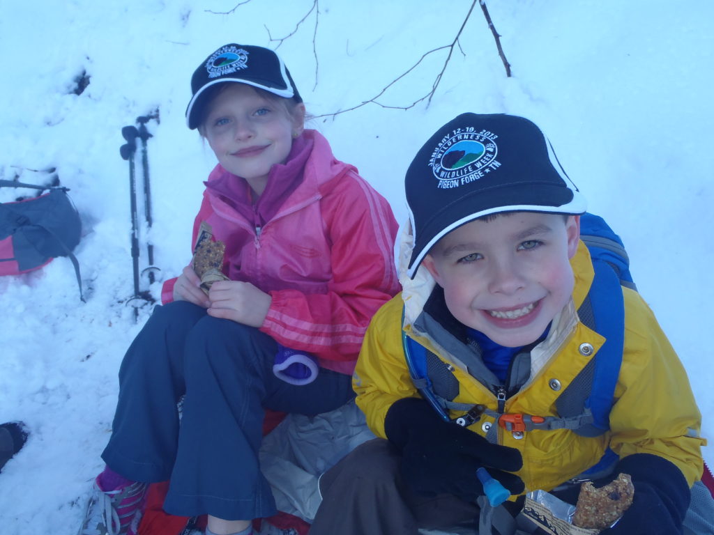 Two children sitting on a hill in the snow.